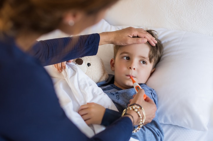 Sick boy with thermometer laying in bed and mother hand taking temperature.