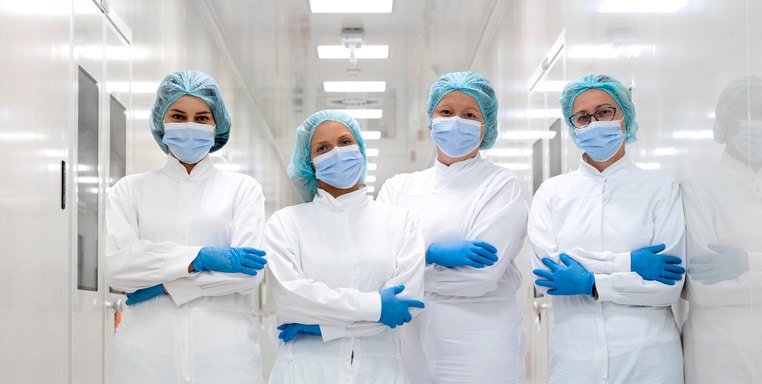 Four female employees in pharmaceutical industry seen in fully protective equipment in the hallway of the production plant of the company of drugs and nutritional supplements during their shift.